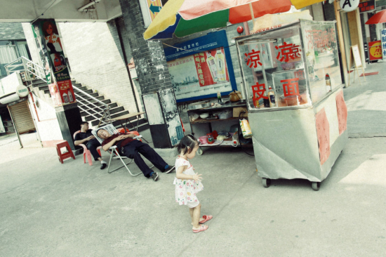 午后的安逸时光：摊主小憩，小女孩独自玩乐。